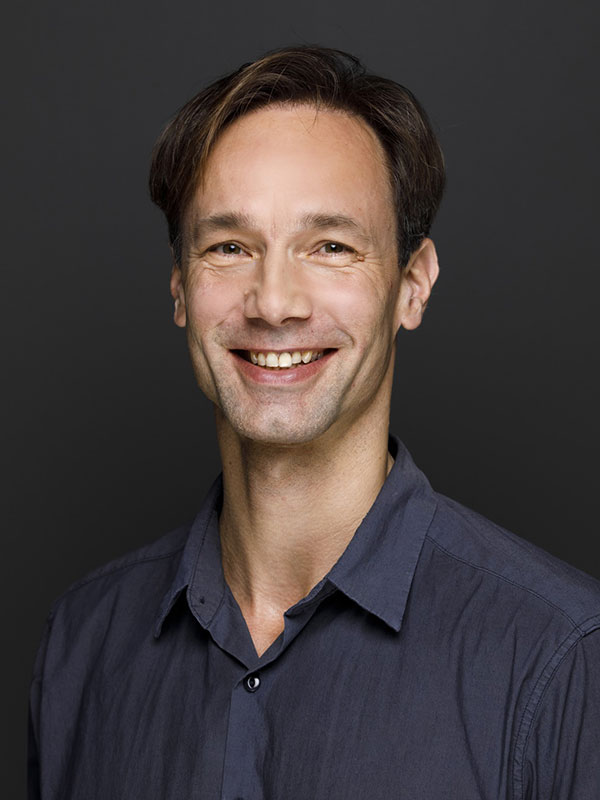 A headshot of Gunther Jikeli, who wears a dark gray dress shirt.